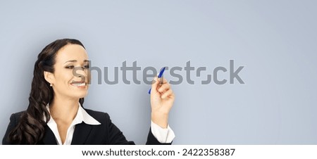 Portrait of happy smiling beautiful young businesswoman in black confident suit, writing or drawing something on screen, by marker. Brunette woman, isolated grey gray wall background