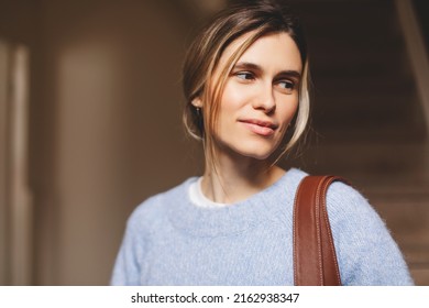 Portrait Of Happy Smiling Blonde Woman Exit Her Home She Go Away With Bag On Shoulder. Blonde Happy Woman With Low Bun Wear Blue Sweater. Young And Beautiful Girl Look At Side.