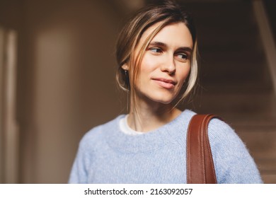 Portrait Of Happy Smiling Blonde Woman Exit Her Home She Go Away With Bag On Shoulder. Blonde Happy Woman With Low Bun Wear Blue Sweater. Young And Beautiful Girl Look At Side.