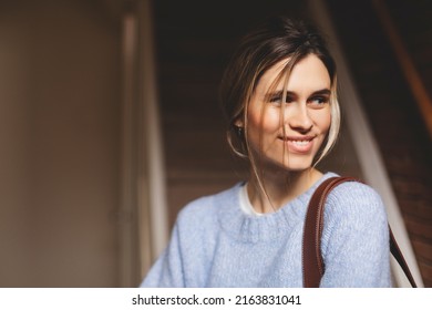 Portrait Of Happy Smiling Blonde Woman Exit Her Home She Go Away With Bag On Shoulder. Blonde Happy Woman With Low Bun Wear Blue Sweater. Young And Beautiful Girl Look At Side.