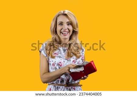 Portrait of happy smiling blonde woman taking money from her wallet. Isolated on yellow.