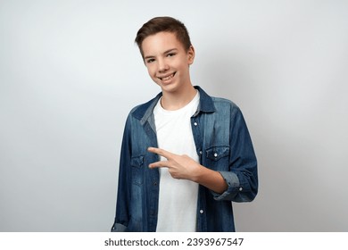 Portrait of happy smiling boy doing victory gesture and looking at camera, showing peace, v sign with double fingers, white background.