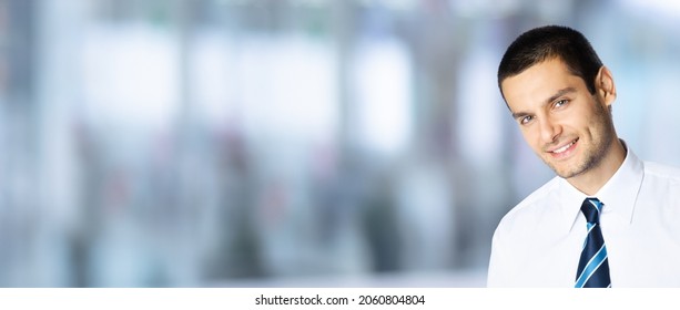 Portrait Of Happy Smiling Brunette Businessman In White Shirt And Tie, Over Blurred Modern Office Interior Background With Copyspace. Confident Business Man Indoors. Male Executive Person Bank Manager