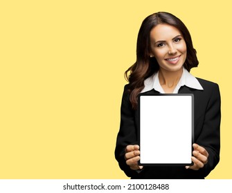 Portrait Of Happy Smiling Brunette Businesswoman Showing Tablet Pc, Touchpad, Ipad With Copy Space For Text, Isolated Over Yellow Colour Background. Confident Beautiful Young Business Woman At Studio