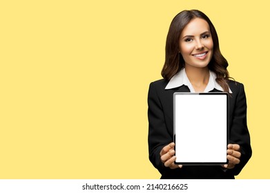 Portrait Of Happy Smiling Brunette Businesswoman Showing Tablet Pc, Touchpad, Ipad With Copy Space Area For Text, Isolate Over Yellow Color Background. Confident Attractive Business Woman At Studio