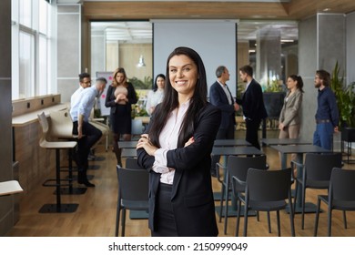 Portrait of happy smiling business teacher and professional team coach. Beautiful woman in suit standing with arms folded in office after corporate training class, with group of workers in background - Shutterstock ID 2150999049