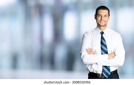 Portrait Of Happy Smiling Businessman In White Shirt And Tie, In Crossed Arm Pose, Over Blurred Modern Office Interior Background. Confident Business Man. Copy Space Area. Male Executive Person.