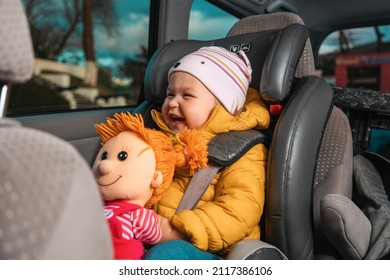 Portrait Of Happy Smiling Caucasian Little Child Is Sitting Strapped In A Child Seat With A Plush Toy In His Hands. View Inside A Car.