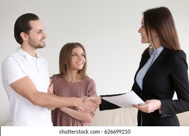 Portrait Of Happy Smiling Couple And Real Estate Broker Shaking Hands, Young Family Meeting With Banker To Discuss Mortgage Loan, Female Advisor Handshaking Clients, Visiting Notary Office 