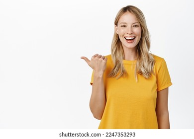 Portrait of happy smiling cute girl, woman pointing finger left at copy space, logo banner, company advertisement, standing against white background - Shutterstock ID 2247353293
