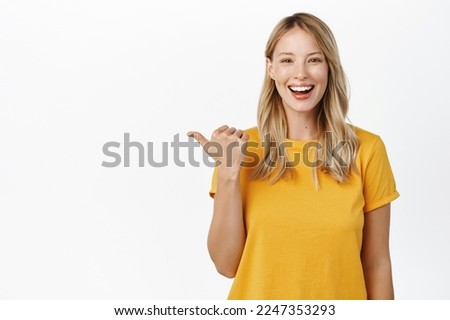 Portrait of happy smiling cute girl, woman pointing finger left at copy space, logo banner, company advertisement, standing against white background