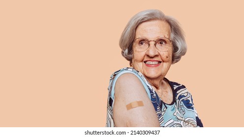 Portrait of a happy smiling elderly grandmother after receiving a vaccine. Elder woman showing her bandaged arm after receiving vaccination. - Powered by Shutterstock