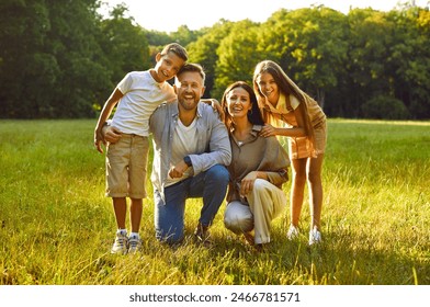 Portrait of happy smiling family of four with son and daughter sitting on green grass in the summer park and looking cheerful at camera. Mother, father with two kids enjoying sunny day together. - Powered by Shutterstock