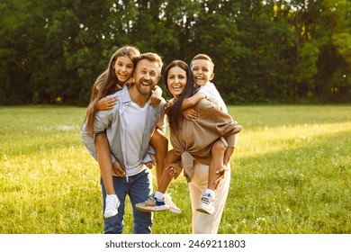 Portrait of happy smiling family of four with son and daughter standing on green grass in the summer park and looking cheerful at camera. Mother, father with two kids enjoying sunny day together. - Powered by Shutterstock