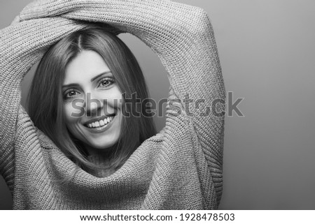 Portrait of happy smiling fashionable model with long blonde hair in gray knitted sweater with hands over head. White shiny smile. Natural make-up. Close up. Studio shot