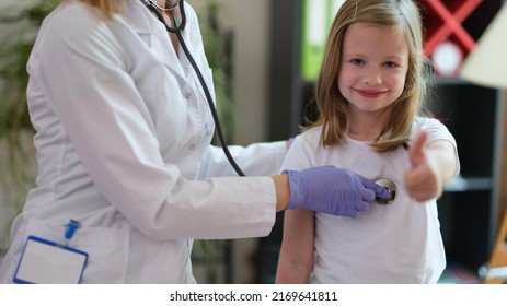 Portrait Of Happy Smiling Girl At Doctor Pediatrician Appointment Showing Thumb Up Sigh. Healthcare, Pediatrics And Medicine Concept