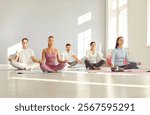 Portrait of happy smiling group of sporty people men and women sitting on the floor on mat and practicing yoga in gym in Lotus pose with closed eyes. Sport and active lifestyle concept.