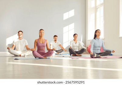 Portrait of happy smiling group of sporty people men and women sitting on the floor on mat and practicing yoga in gym in Lotus pose with closed eyes. Sport and active lifestyle concept.