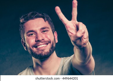 Portrait Of Happy Smiling Handsome Man Guy Giving Peace Victory V Sign Gesture In Studio On Black.