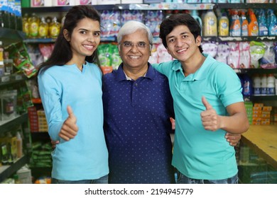 Portrait Of Happy And Smiling Indian Grand Father Purchasing In A Grocery Store With The Young Grand Children. Buying Grocery For Home In A Supermarket. Cheerful And Joyful Family Doing Thumbs Up.