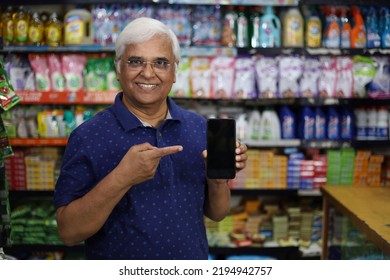 Portrait of Happy and smiling Indian mid aged man purchasing in a grocery store pointing towards the mobile app. Buying grocery for home in a supermarket. Cheerful and joyful man doing thumbs up. - Shutterstock ID 2194942757