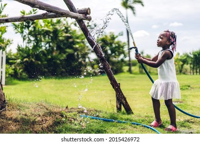 Portrait of happy smiling little child african american girl playing and watering garden grass with rubber strap and sunny summer in garden at home - Powered by Shutterstock