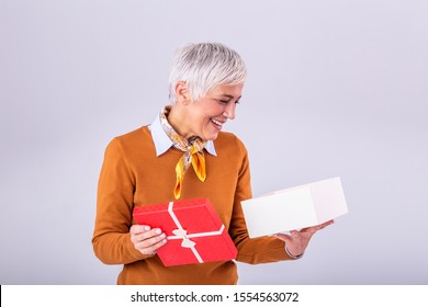 Portrait Of A Happy Smiling Mature Woman Opening A Gift Box Isolated Over Gray Background. Excited Senior Casual Woman Holding Present Box