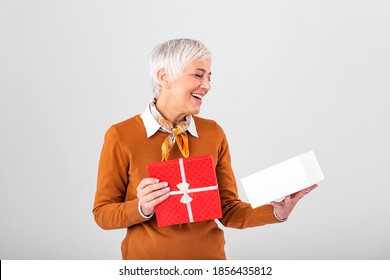 Portrait Of A Happy Smiling Mature Woman Opening A Christmas Gift Box Isolated Over Gray Background. Excited Senior Casual Woman Holding Present Box