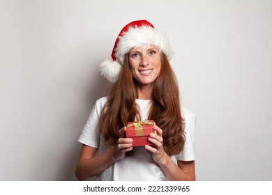 Portrait Of Happy Smiling Mature Woman In Christmas Hat Holding Red Gift Box On White Studio Wall Background