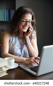 Porträt einer glücklich lächelnden reifen Frau in Brillen, die telefonisch spricht und zu Hause auf Laptop arbeitet