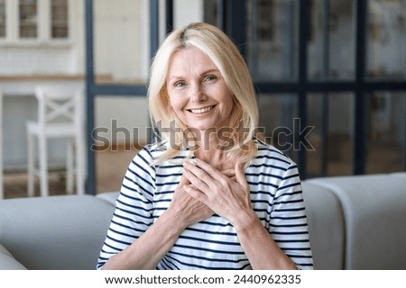 Portrait of happy smiling mature woman holding hands on chest, feeling grateful, thankful, appreciation. Female showing gratitude, love, faith and believe