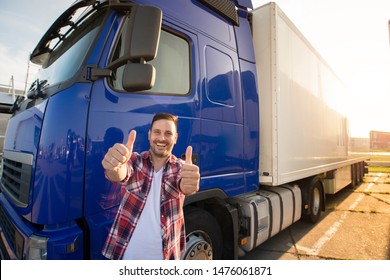 Portrait of happy smiling middle aged truck driver standing by his truck and holding thumbs up. Successful transportation service.