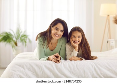 Portrait of happy, smiling mother and child in bedroom. Good looking young mum together with pretty little daughter cuddling on cosy, warm, comfortable bed. Concept of family, love, care and comfort