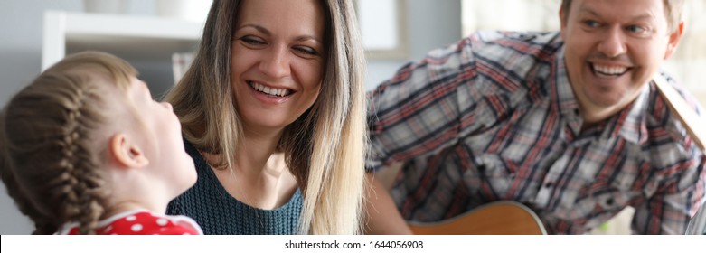 Portrait of happy smiling parents and daughter spending time together. Mom, father looking at kid with happiness. Mum, daddy and child playing on musical instruments. Parenthood and childhood concept - Powered by Shutterstock