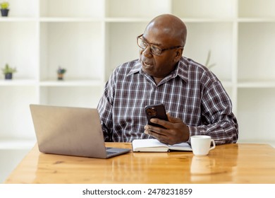 Portrait of happy smiling senior man sitting on desk at cafe using smartphone and laptop - Powered by Shutterstock