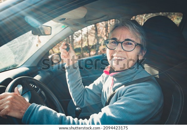 Portrait of a happy smiling senior woman learning\
to drive a car holding the car key to camera.Safety drive.Learning\
new hobby,habit and skill for this new year.Old person approving\
driving license