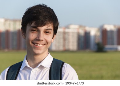 Portrait Of A Happy Smiling Teenager With A Backpack, A School Teenager Waiting For A School Bus, On His Way To School. On The Way Home From School Against The Background Of The Urban Landscape