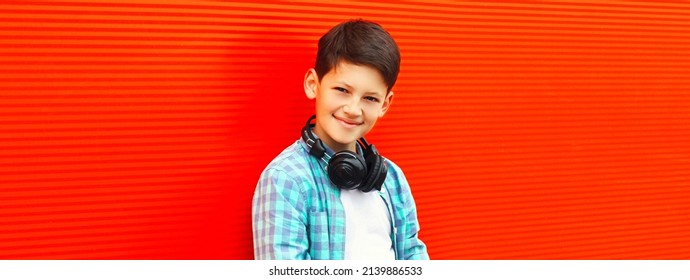 Portrait eines glücklich lächelnden Teenagerjungen, der Musik in Kopfhörern auf rotem Hintergrund hört