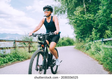 Portrait of a happy smiling woman dressed in cycling clothes, helmet and sunglasses riding a bicycle on the asphalt out-of-town bicycle path. Active sporty people concept image.