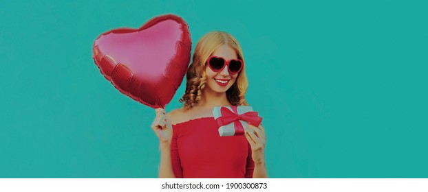 Portrait Of Happy Smiling Woman With Gift Box And Red Heart Shaped Balloon On A Blue Background