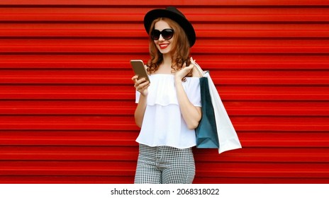 Portrait of happy smiling woman with shopping bags and smartphone on colorful red background - Shutterstock ID 2068318022