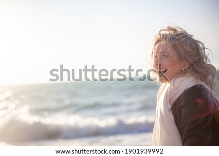 Portrait of happy smiling woman walking outdoor in the sea shore beach on wind weather against the sun lights.