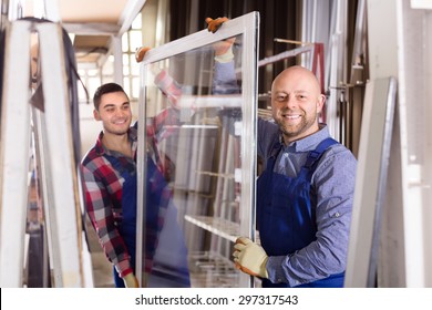 Portrait of happy smiling workers in coverall working with PVC window at factory
