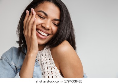 Portrait of a happy smiling young african woman with long dark hair wearing casual clothes standing isolated over gray background - Shutterstock ID 1794008428
