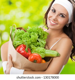 Portrait Of Happy Smiling Young Beautiful Woman In Fitness Wear Holding Grocery Shopping Bag With Healthy Vegetarian Food, Outdoors