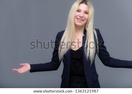 Portrait of happy smiling young cheerful businesswoman standing. Success in business concept studio shot talking to a client. Gray suit. Young female model. Gray wall background. Looking at camera.