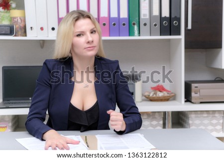 Portrait of happy smiling young cheerful businesswoman sitting in office. Success in business concept studio shot talking to a client. Blue suit. Female model. Gray wall background. Looking at camera.