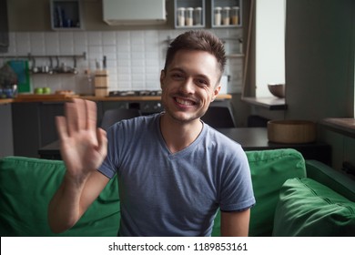 Portrait happy smiling young man waving hand, looking at camera, greeting, saying hello, head shot portrait