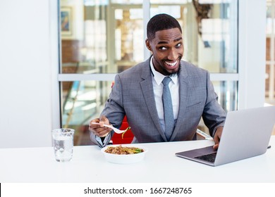 Portrait of a happy smiling young man in business suit eating lunch at work at his desk with laptop computer in his office - Powered by Shutterstock