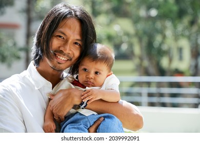 Portrait of happy smiling young man holding cute baby boy when standing outside on sunny summer day